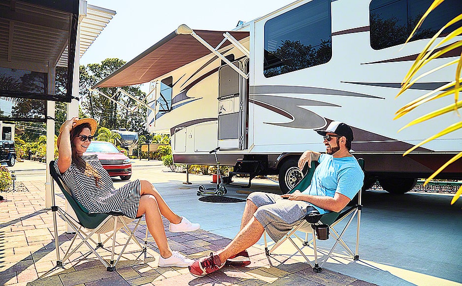 Young couple sits on chairs near camping trailer and car | SiteMindWeb